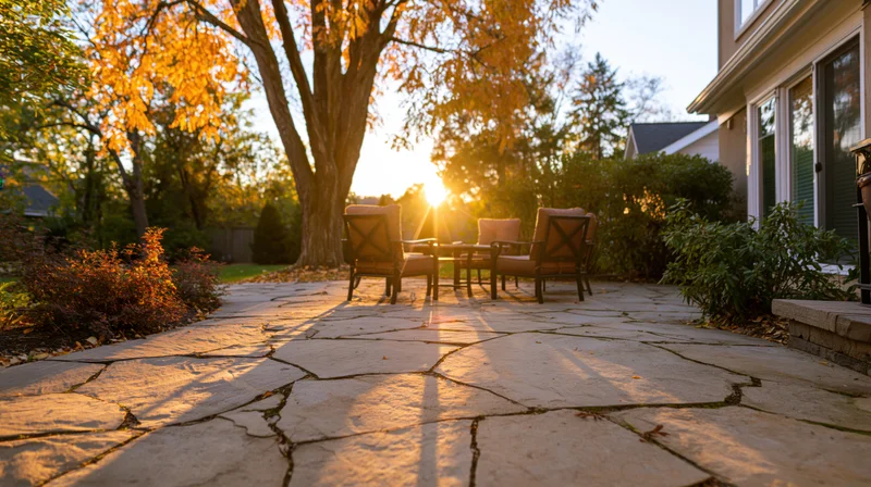 Stone patio with wooden chairs and table in suburban backyard at golden hour during autumn