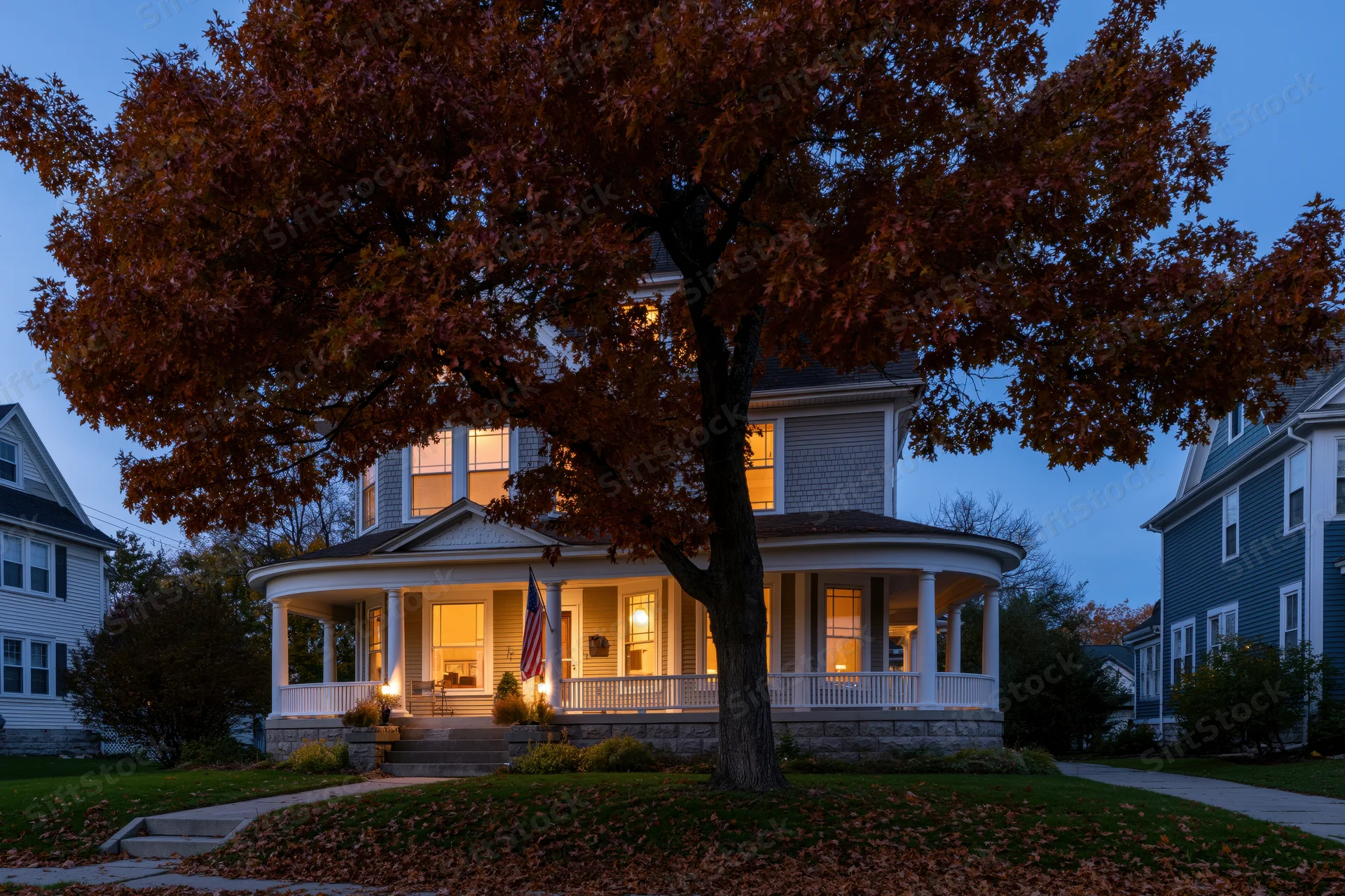 Victorian house with wraparound porch and autumn tree in front at twilight
