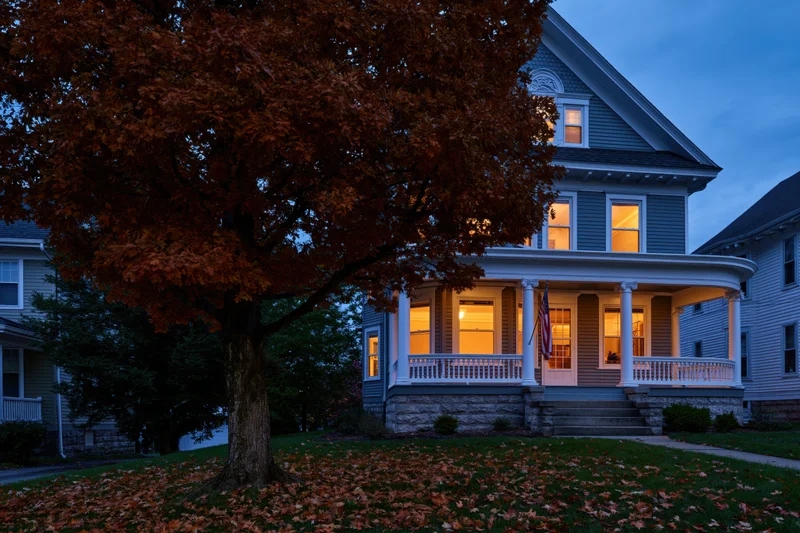 Victorian house with wraparound porch and autumn foliage at twilight