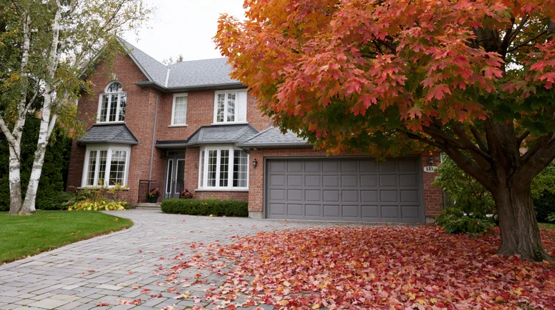 Two-story brick suburban house with autumn leaves on the driveway and front yard