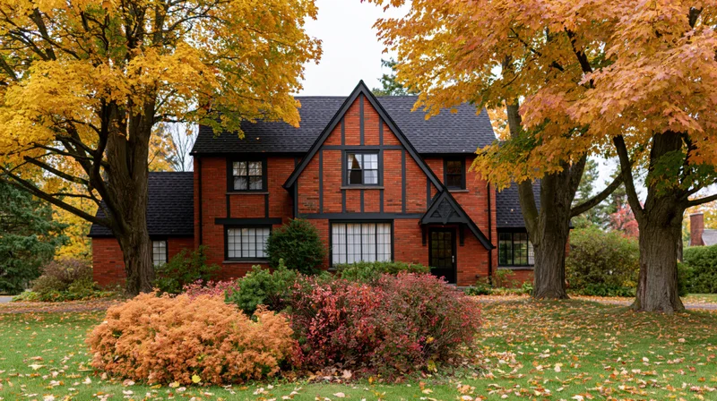 Red brick cottage-style house with dark trim surrounded by autumn trees and colorful foliage in front yard