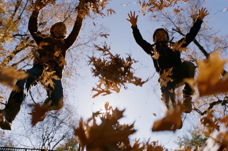Two children jumping and tossing autumn leaves in a park under a blue sky