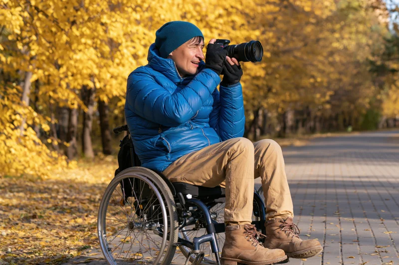 Man in wheelchair photographing autumn trees in park