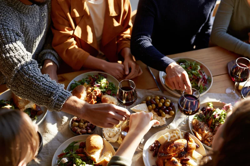 People sharing a meal at a sunlit outdoor dinner party with wine and food on a wooden table