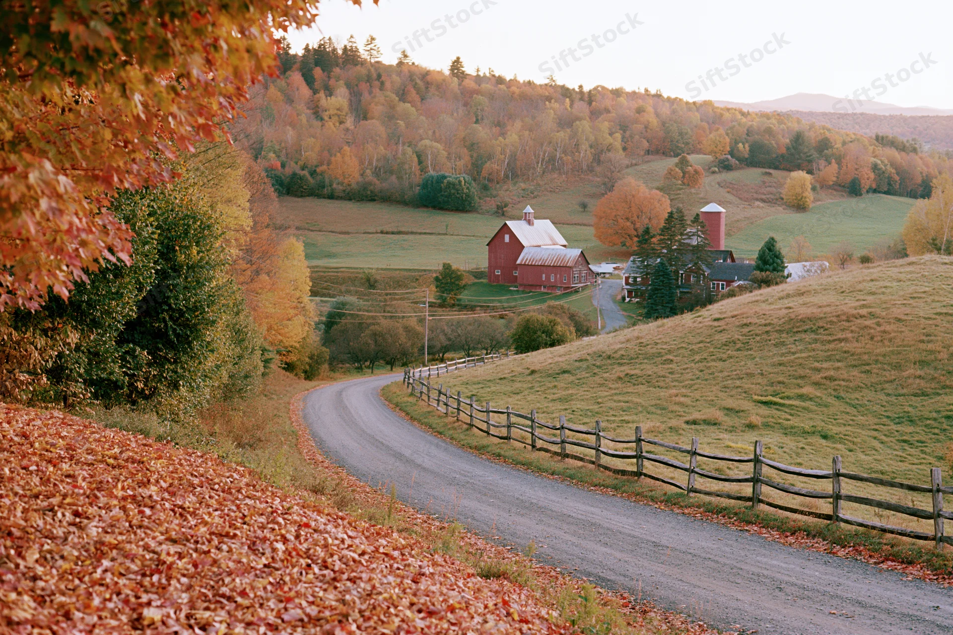 Winding road through autumn foliage leading to a red barn on a Vermont hillside farm
