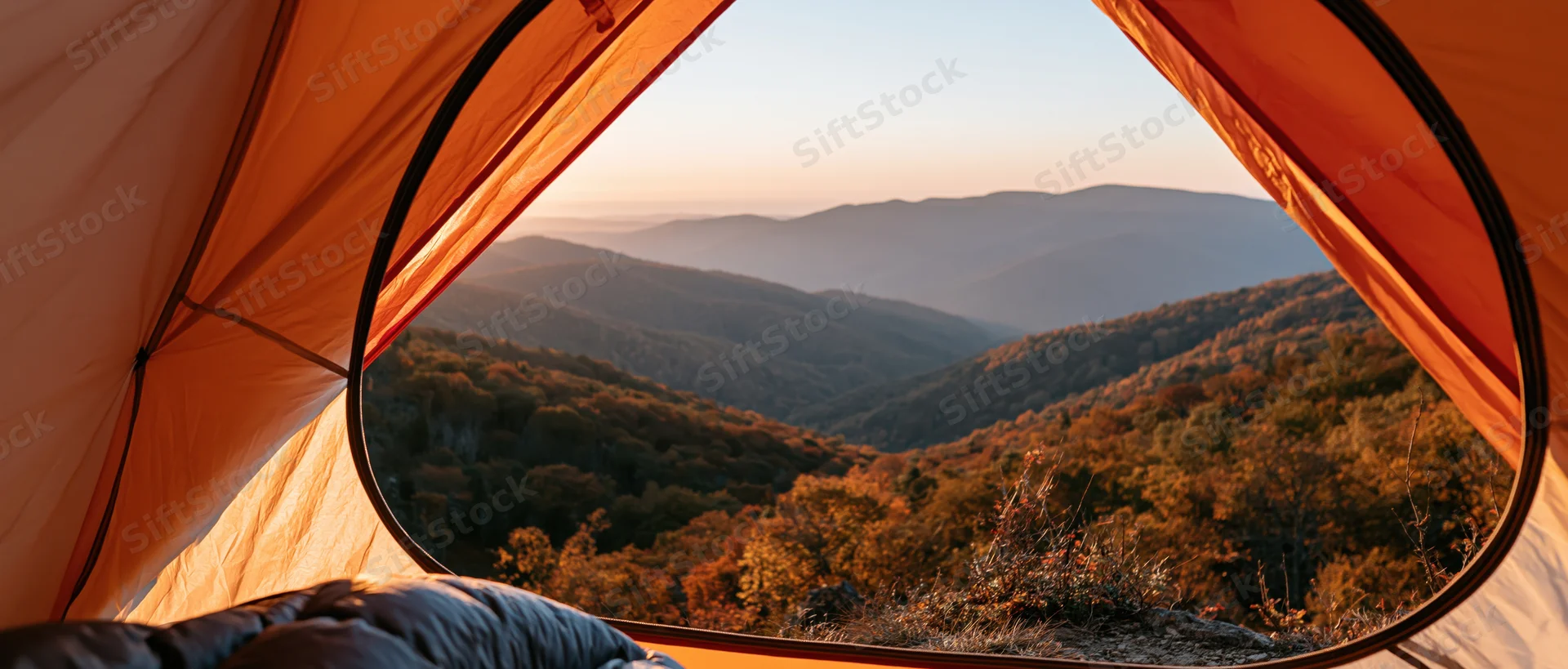 View from inside an orange tent looking out over a mountain valley at sunrise