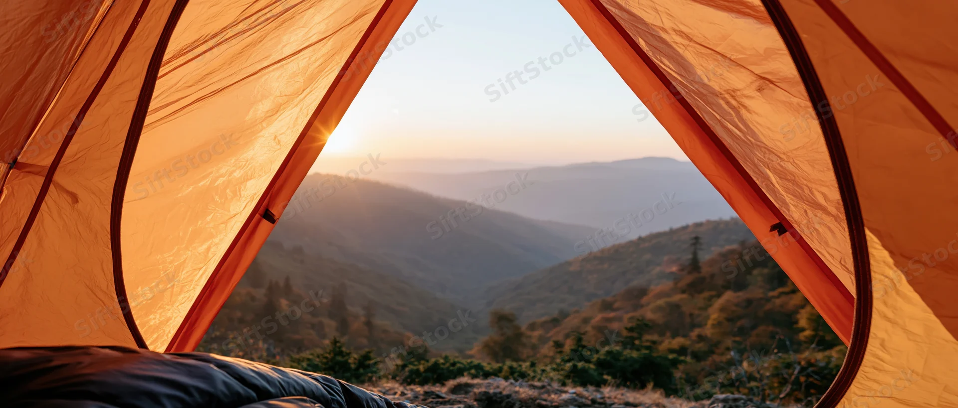 View from inside an orange tent looking out over a mountain valley at sunrise