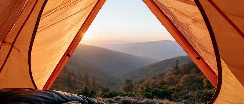 View from inside an orange tent looking out over a mountain valley at sunrise