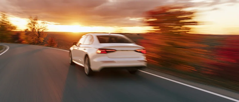 White sedan driving away on a country road at sunset