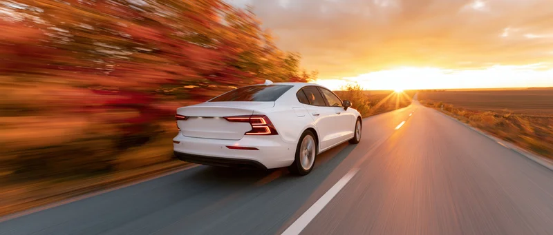 White sedan driving away on a straight country road at sunset