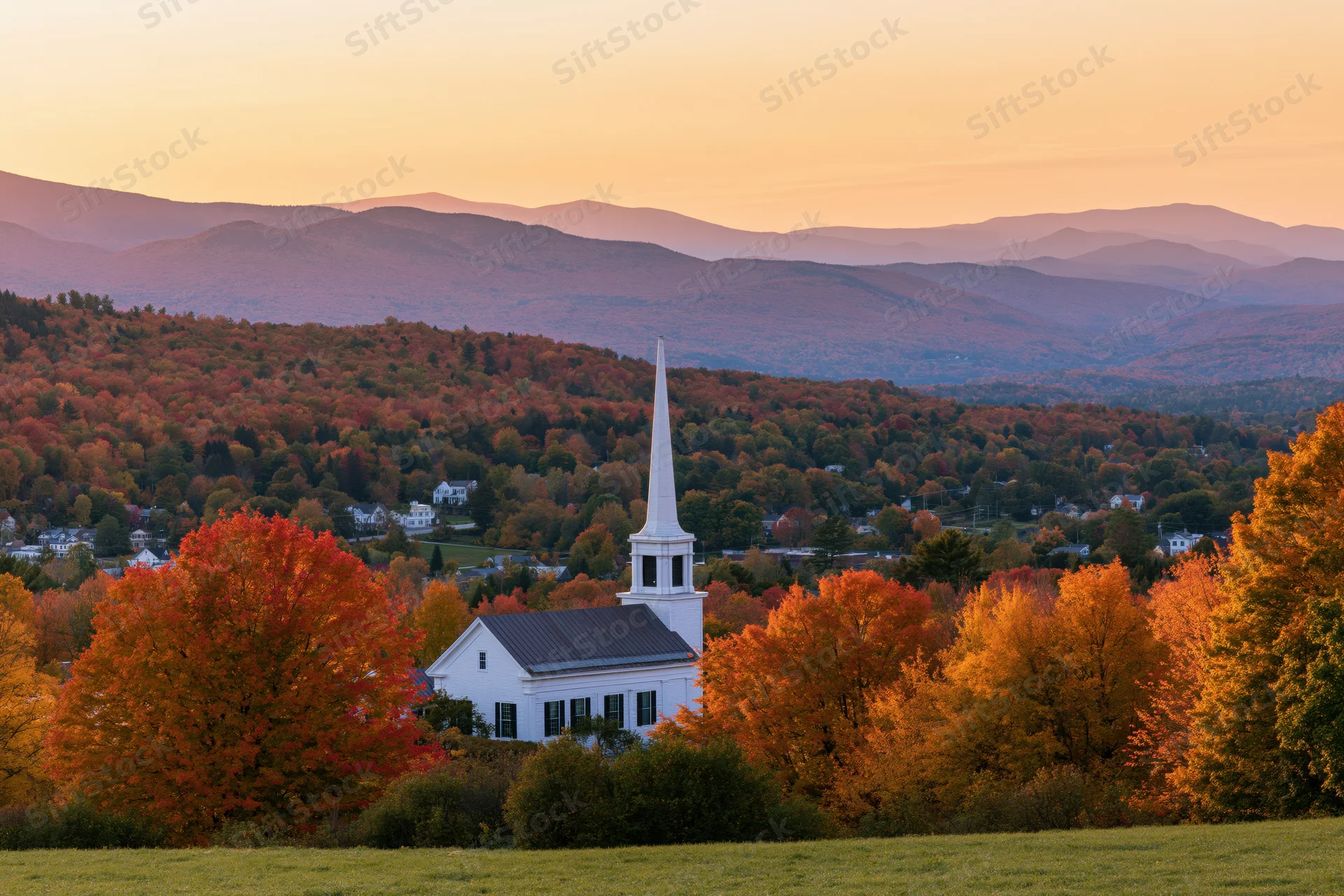 White church with steeple rising above autumn trees in a rural valley at sunset
