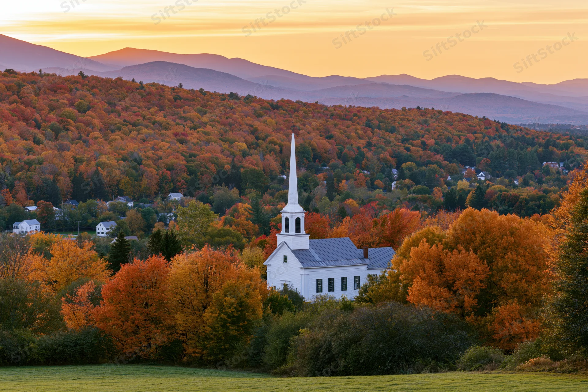 White new england church with steeple surrounded by autumn foliage in a rural valley at sunset