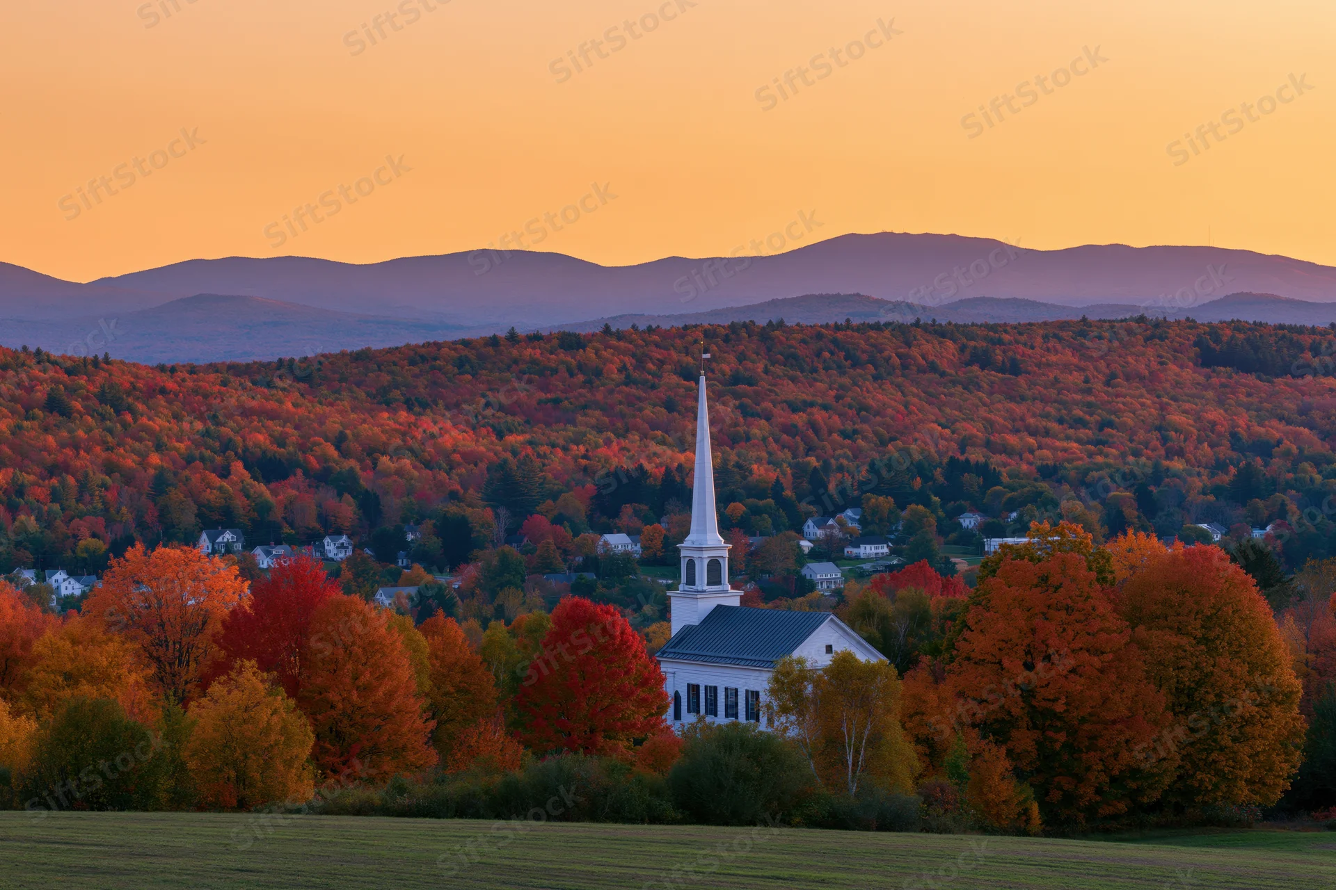 White church steeple rising above autumn foliage in a rural new england landscape at sunset