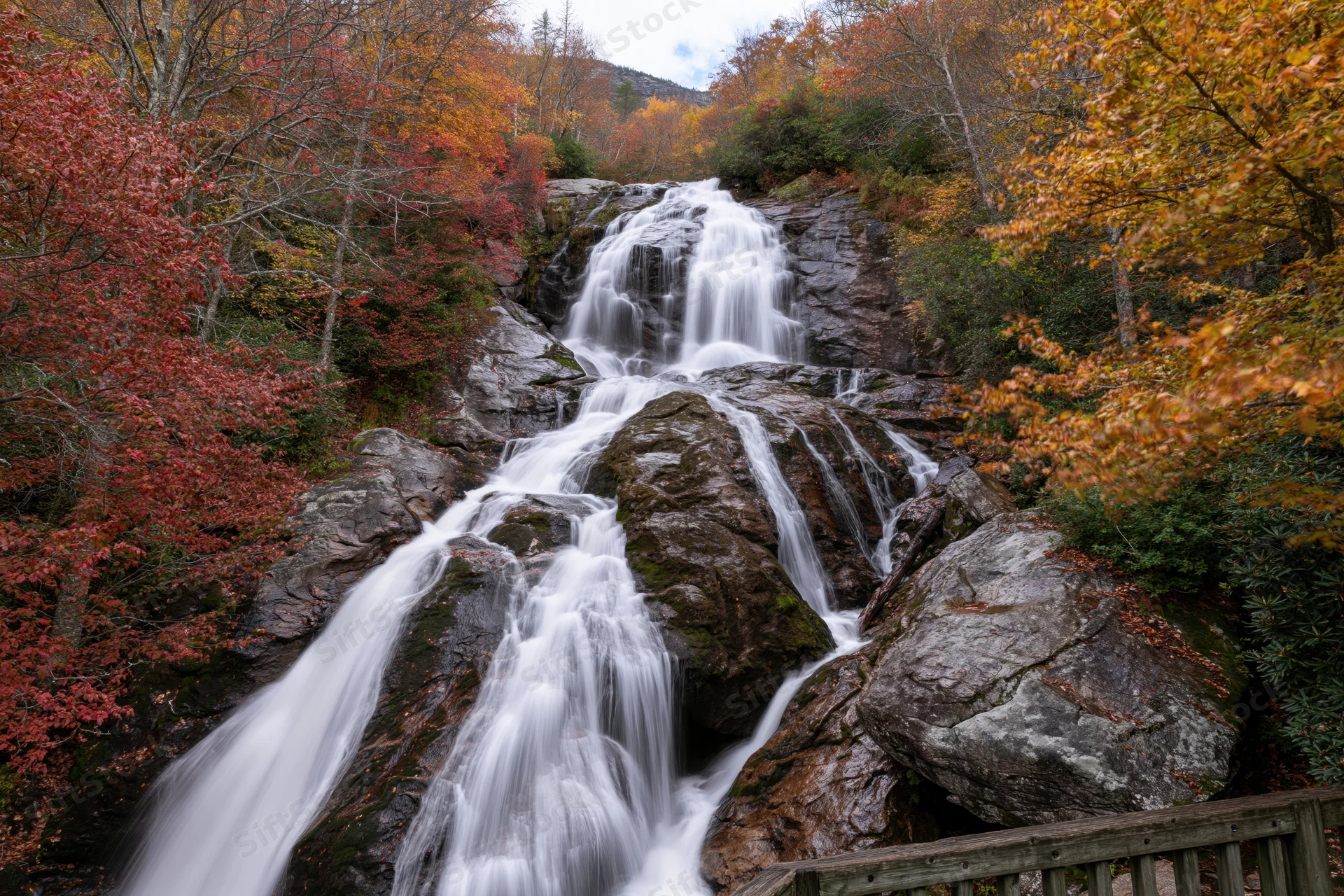 Cascading waterfall flowing over mossy boulders in autumn forest