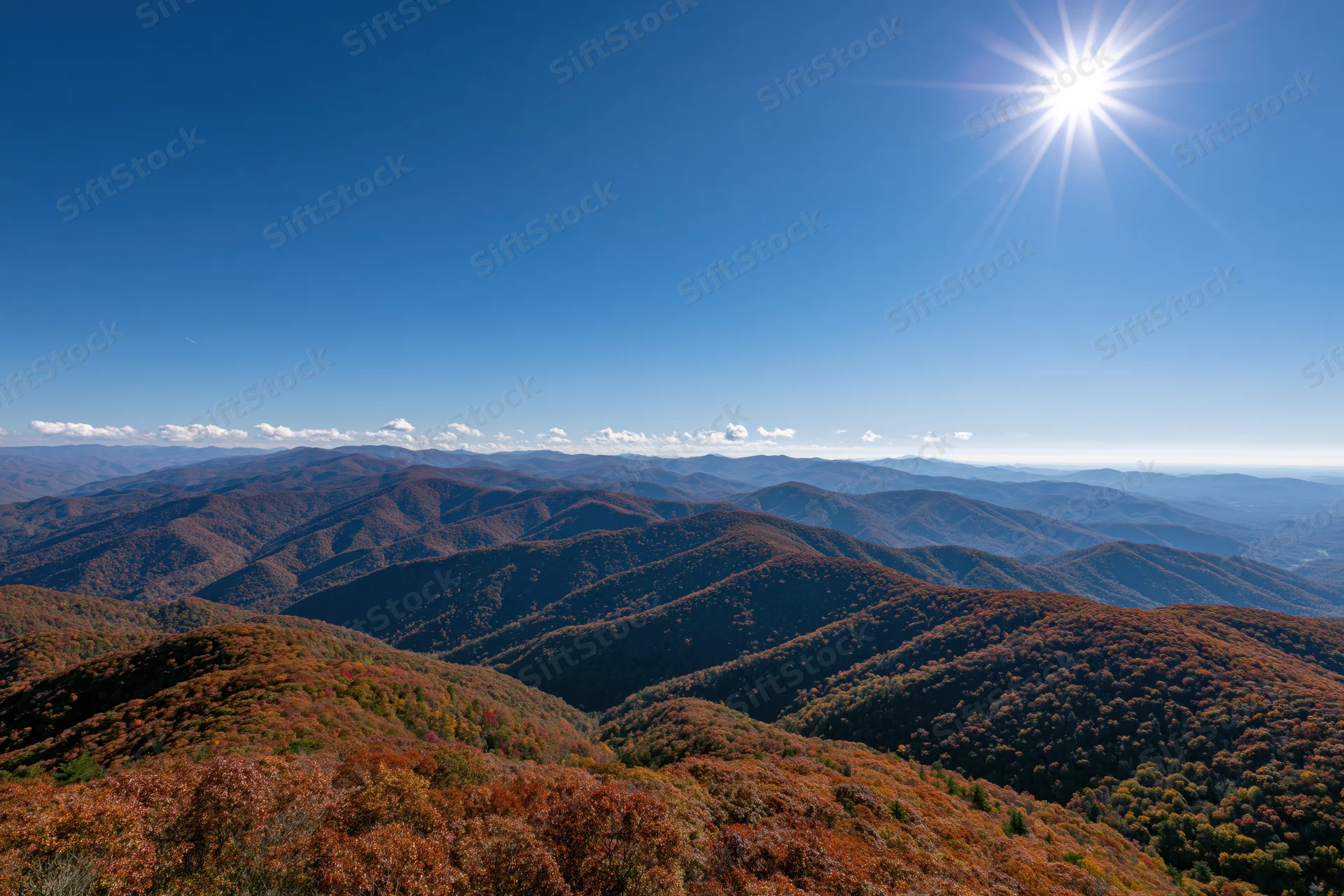 Rolling mountain ridges covered in autumn foliage under a clear blue sky with bright sun