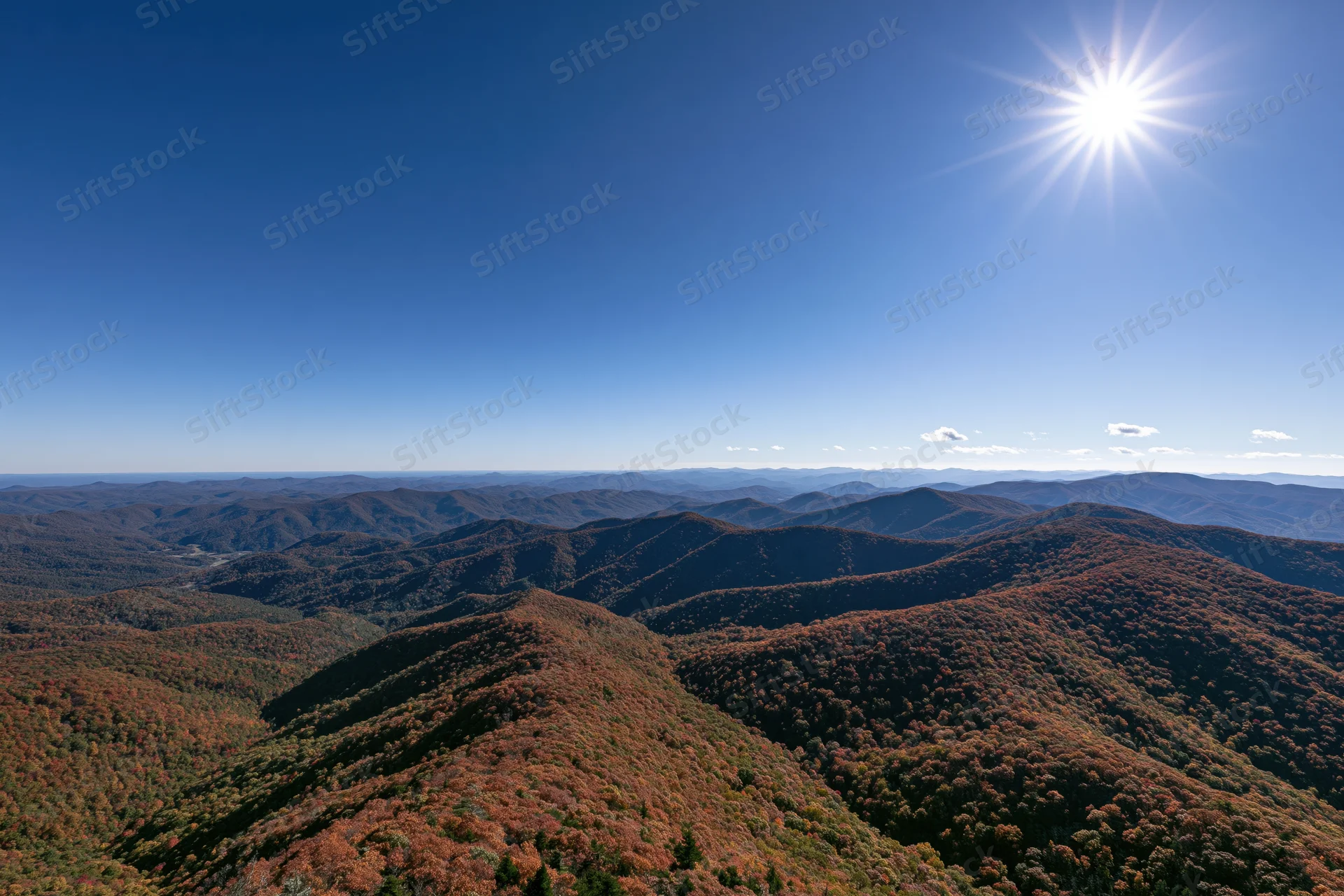 Rolling mountain ridges covered in autumn foliage under a clear blue sky with bright sun
