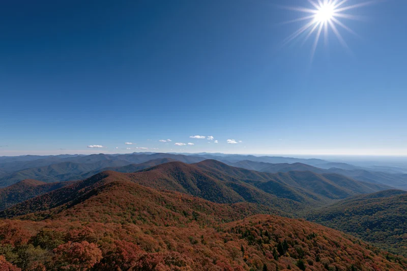 Rolling mountain ridges covered in autumn foliage under a bright sun and clear blue sky