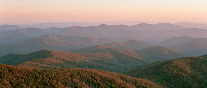 Panoramic view of rolling forested mountains at sunset with layered hills and autumn foliage