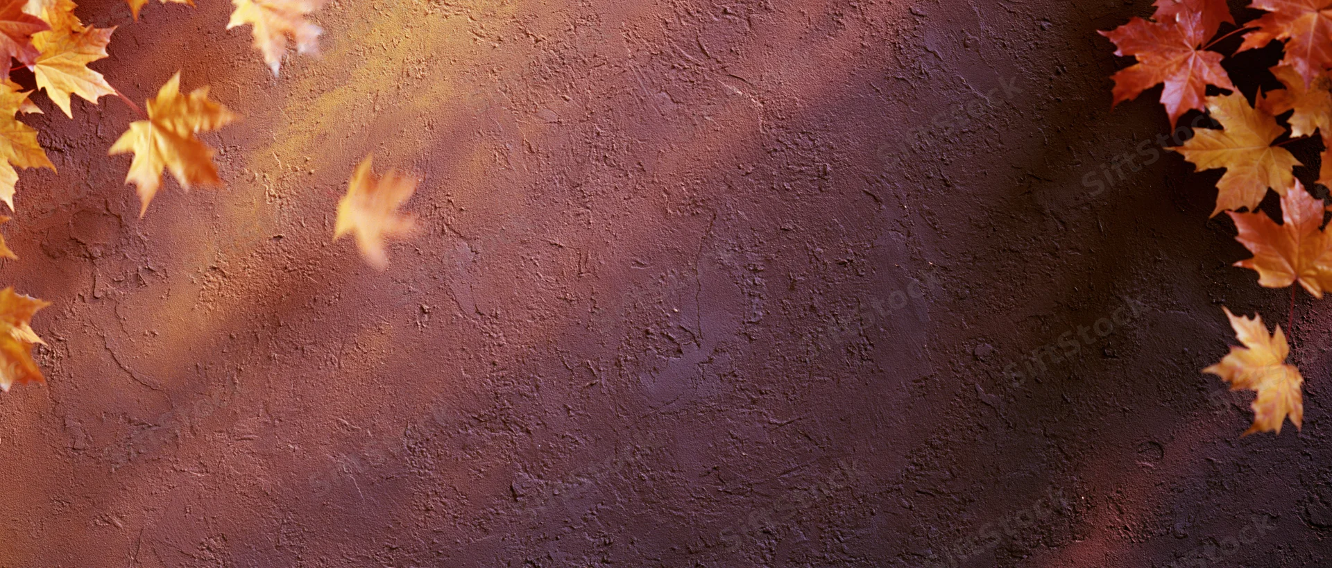 Autumn maple leaves arranged along the edges of a textured brown surface with copyspace in the center