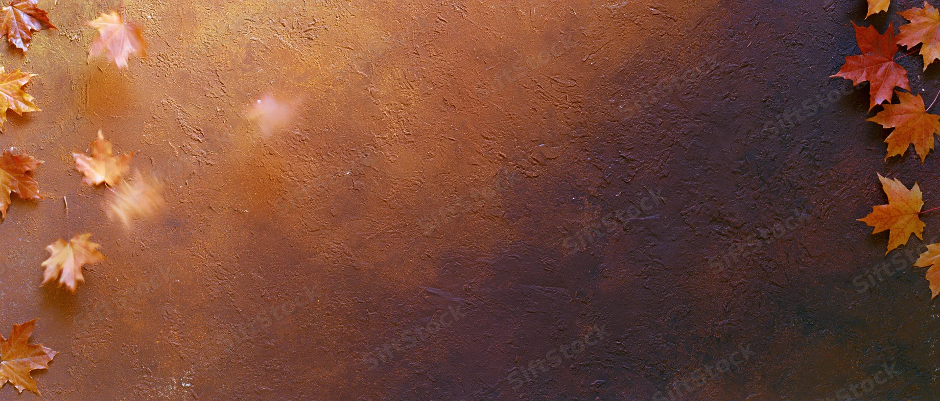 Autumn maple leaves scattered on a textured brown surface with copyspace
