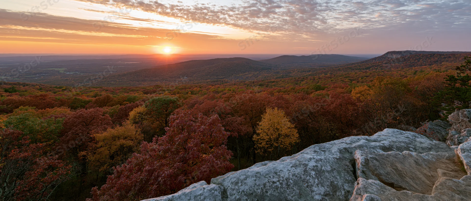 Panoramic view from rocky overlook across autumn forest at sunset