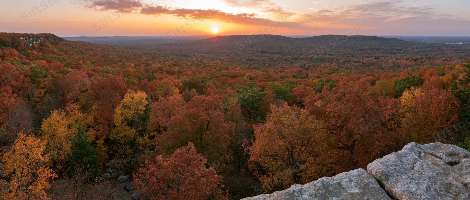 Panoramic view from rocky overlook across autumn forest at sunset