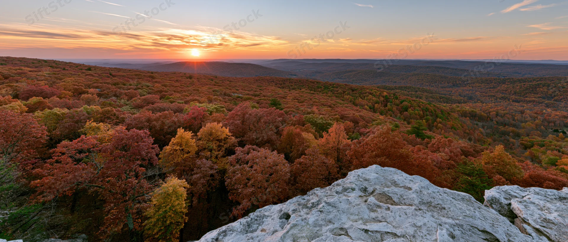 Panoramic view from rocky overlook across autumn forest at sunset