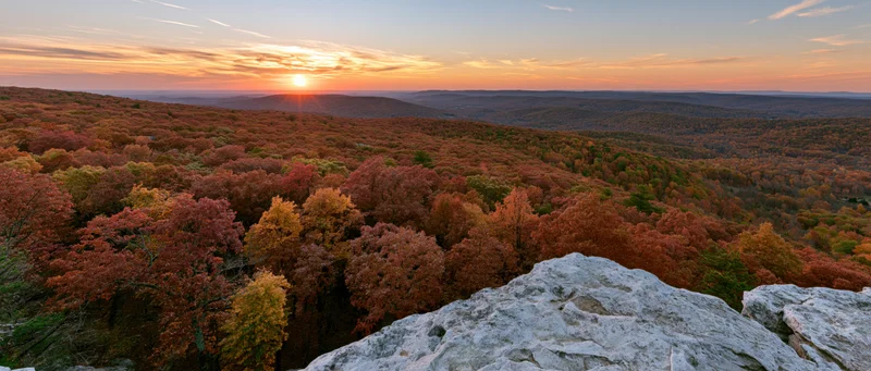 Panoramic view from rocky overlook across autumn forest at sunset