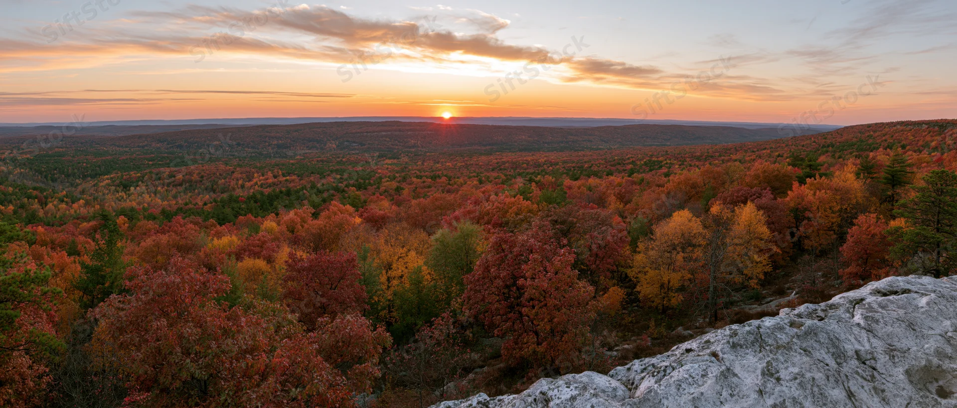 Panoramic view from rocky overlook across autumn forest at sunset
