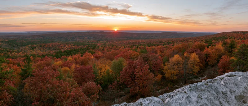 Panoramic view from rocky overlook across autumn forest at sunset