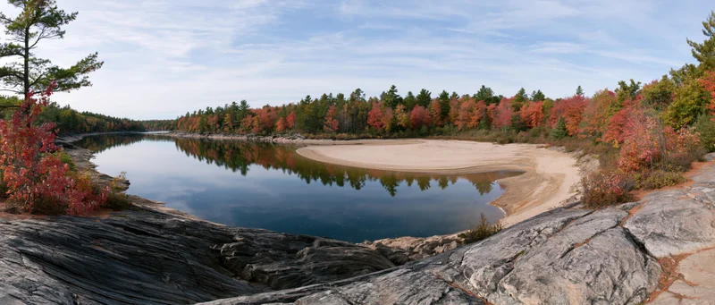 Calm river bend reflecting autumn foliage surrounded by rocky shore and forest