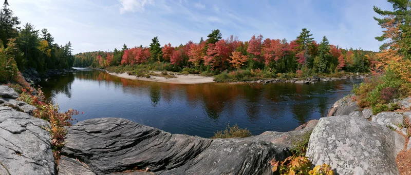 Calm river bend surrounded by autumn-colored trees and rocks under a blue sky