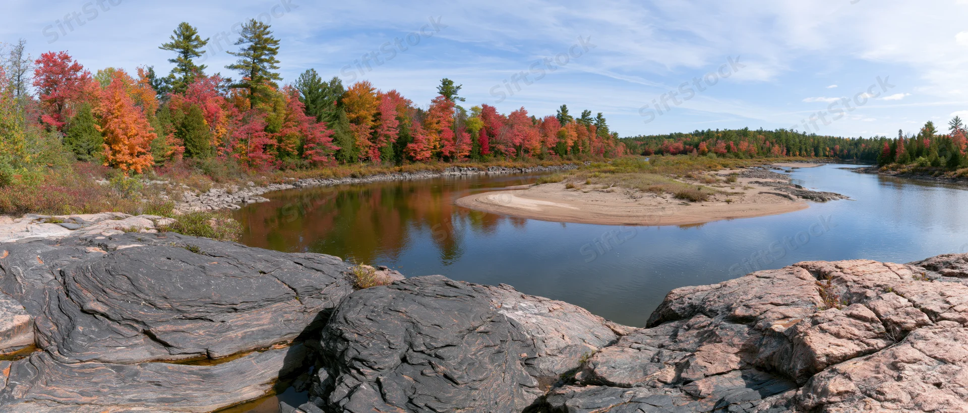 Calm river bend curving through autumn forest with colorful foliage reflected in water, surrounded by rocks and trees