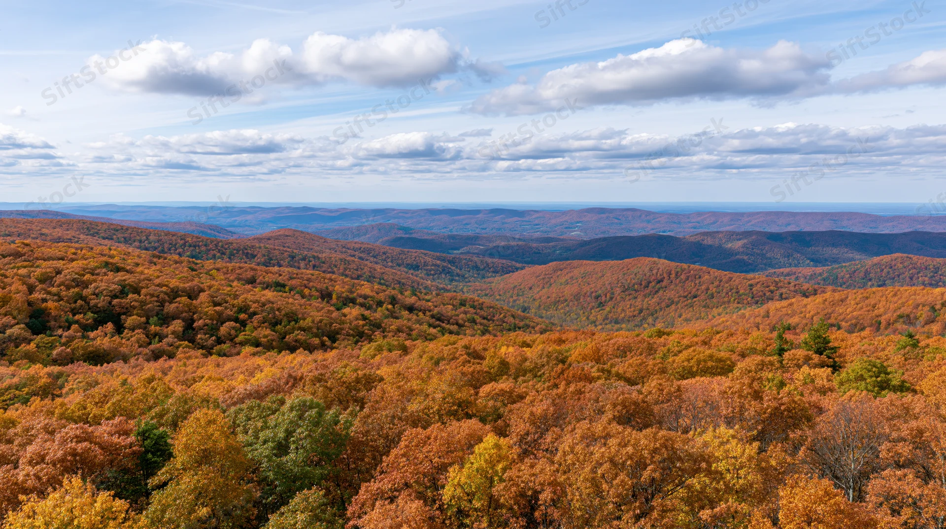 Panoramic view of rolling forested hills covered in autumn foliage under a partly cloudy sky