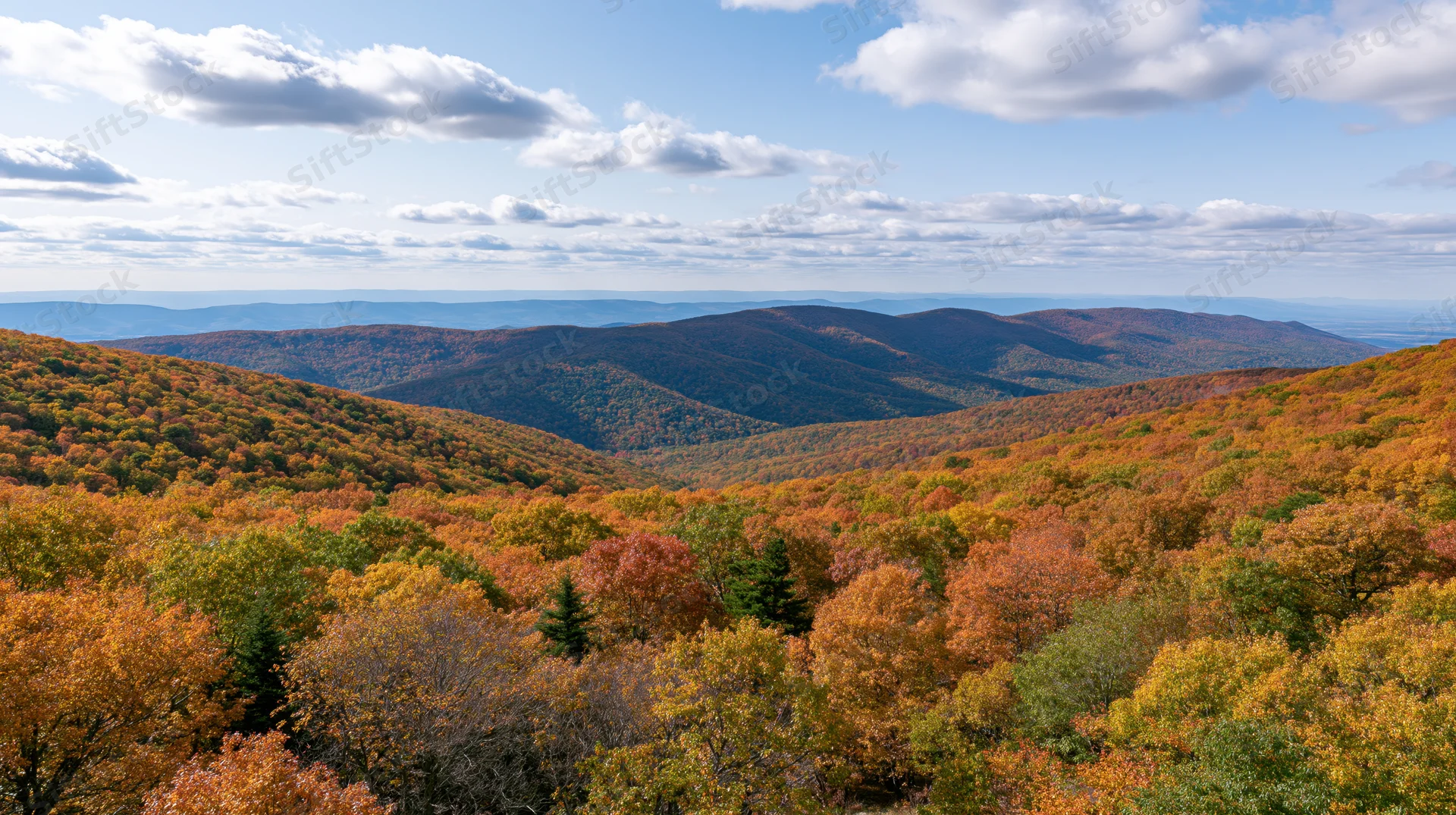 Panoramic view of rolling forested hills covered in autumn foliage under a partly cloudy sky
