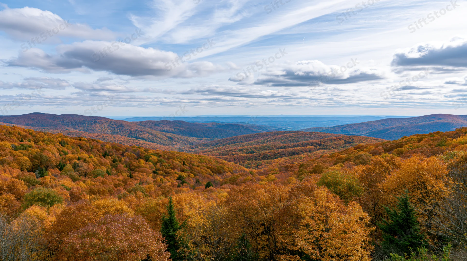 Panoramic view of rolling forested hills covered in autumn foliage under a partly cloudy sky