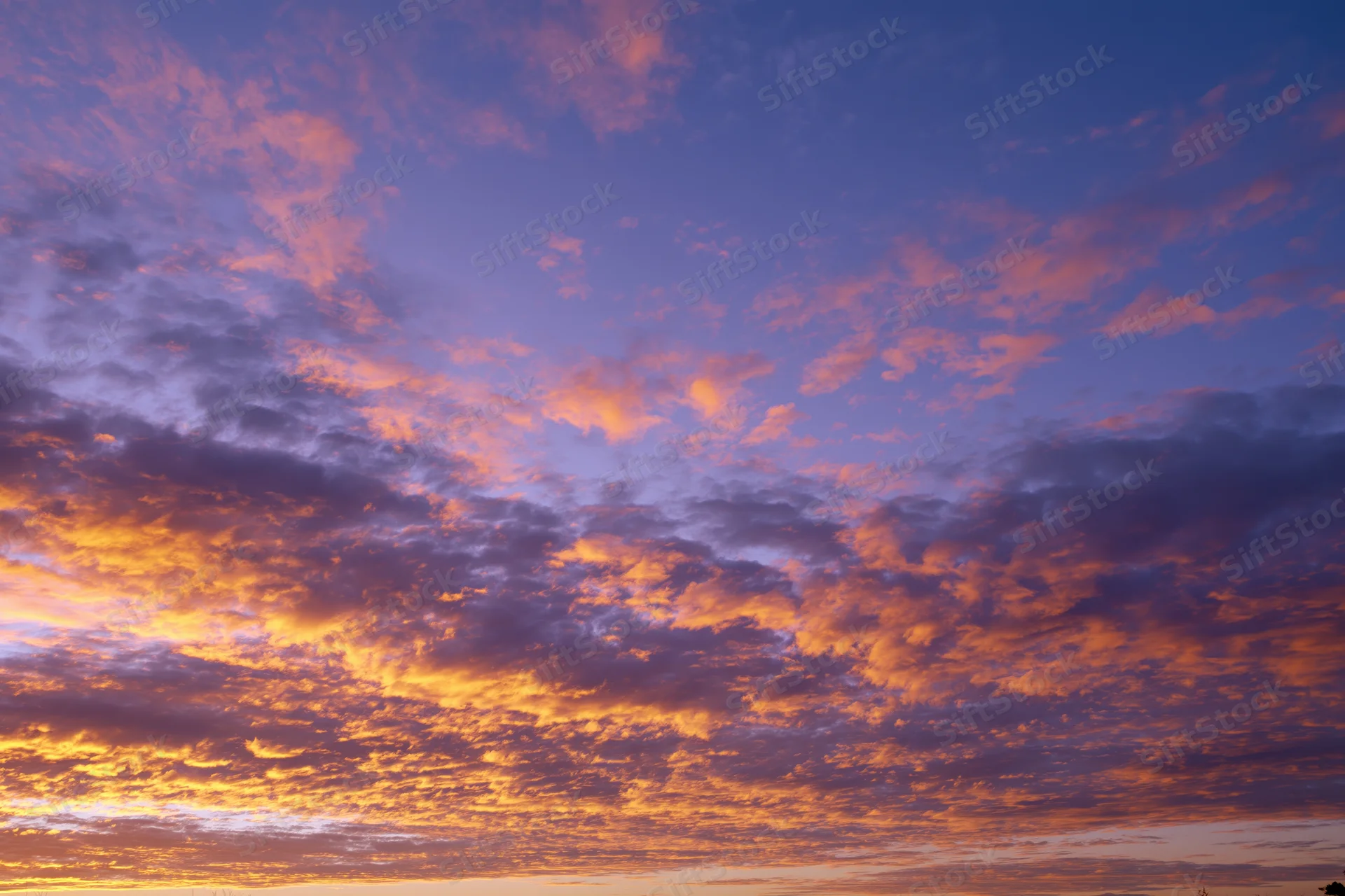 Dramatic sunset sky filled with orange and pink clouds against a deep blue twilight background