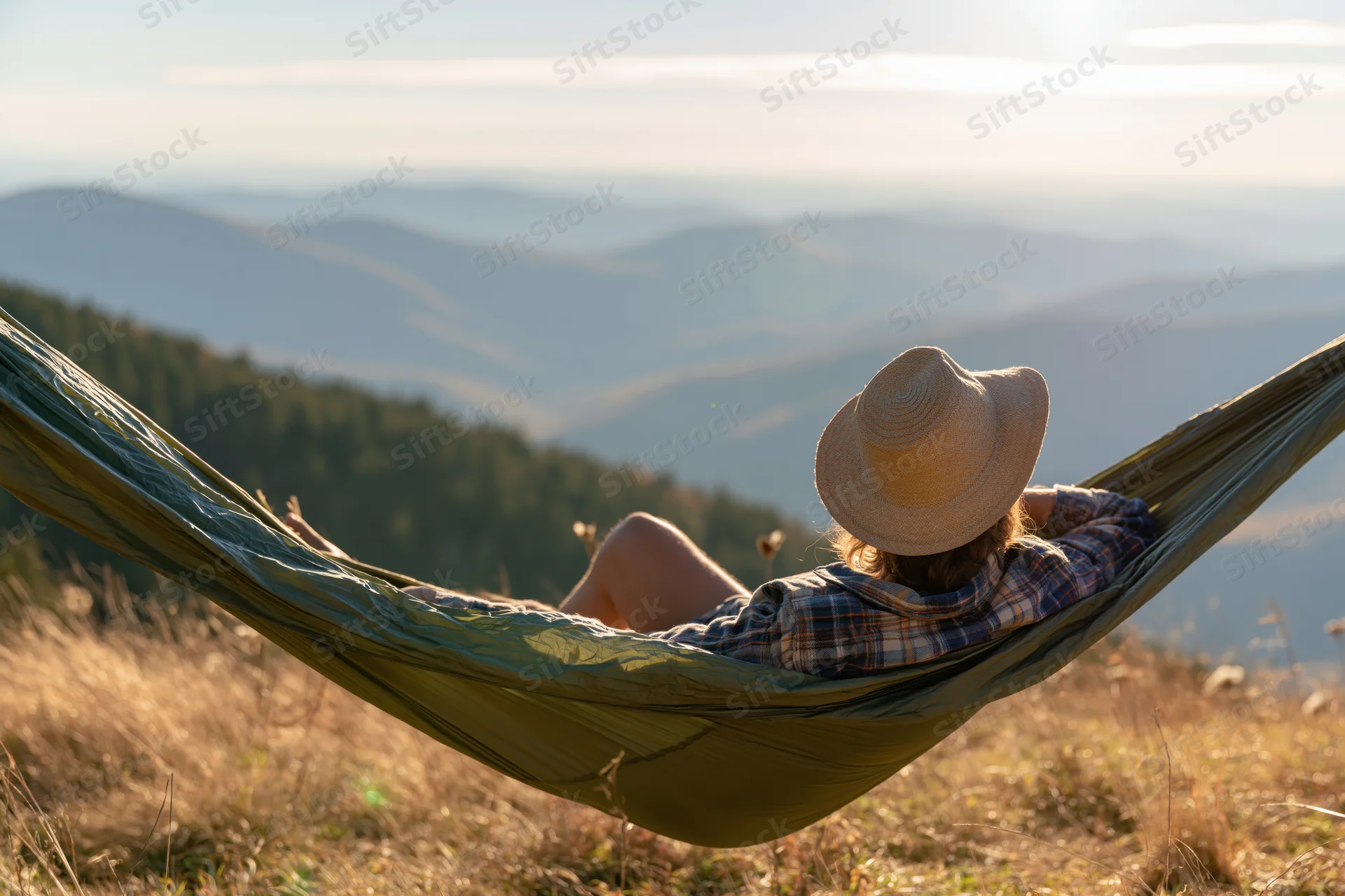 Woman reclining in green hammock overlooking mountain valley at golden hour