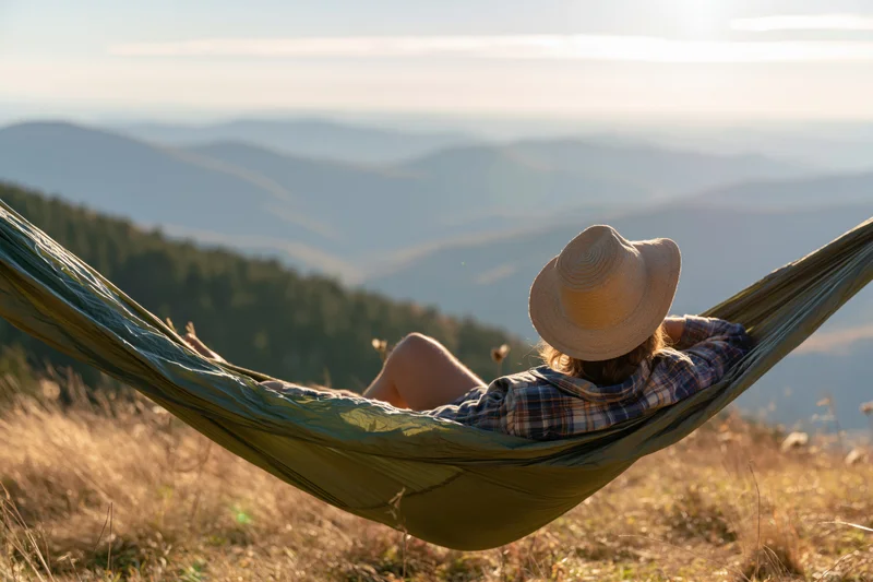 Woman reclining in green hammock overlooking mountain valley at golden hour