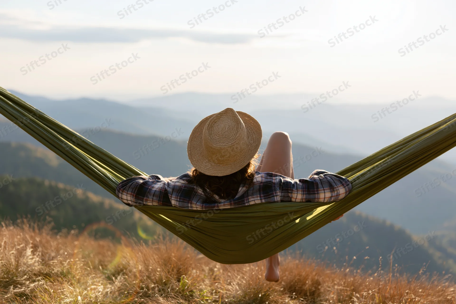 Woman reclining in green hammock on mountain hillside overlooking valley at sunset