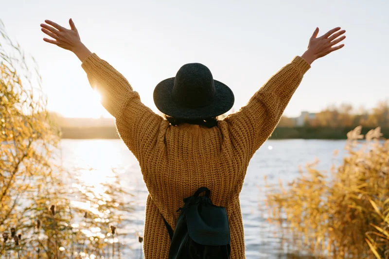 Woman with arms raised standing by lake at sunset