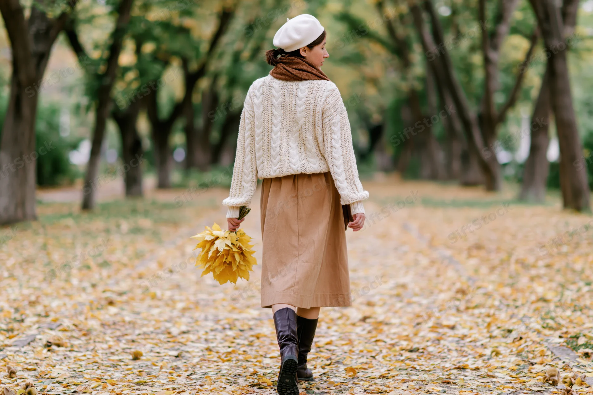 Woman walking down a leaf-covered path in a park during autumn