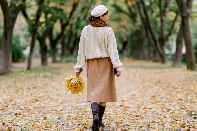 Woman walking down a leaf-covered path in a park during autumn