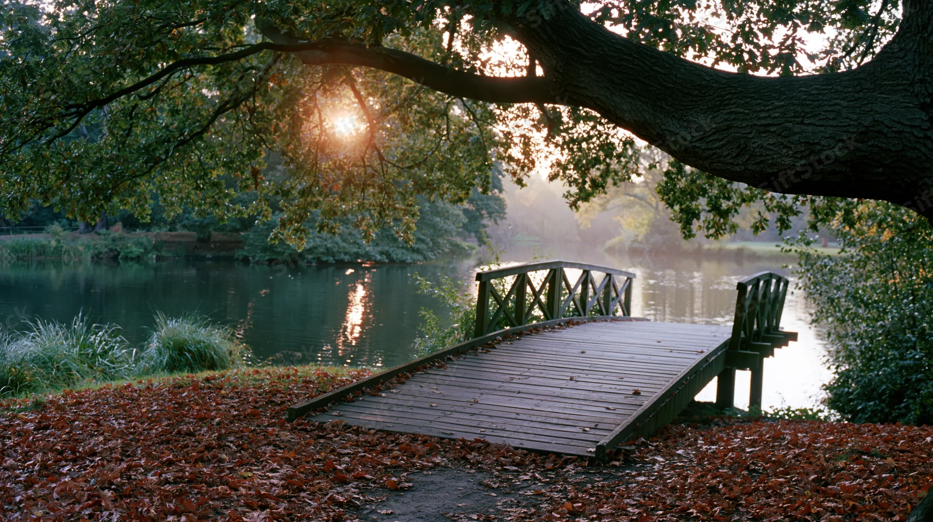 Wooden footbridge over calm pond in autumn park at sunset