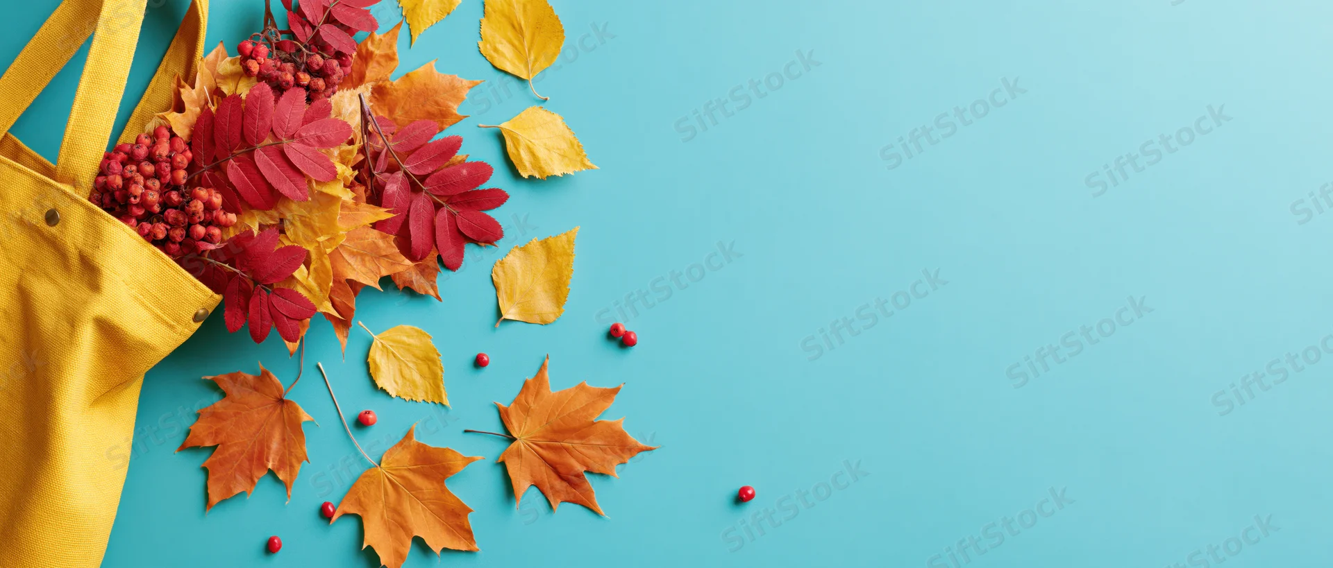 Yellow canvas tote bag overflowing with autumn leaves and red berries on blue background