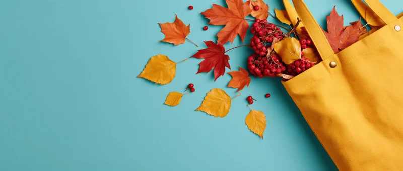 Yellow canvas tote bag overflowing with autumn leaves and red berries on blue background