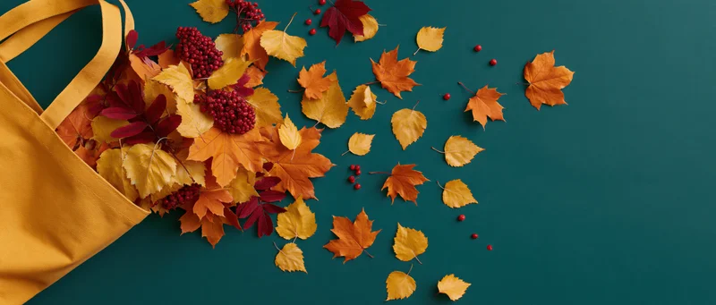 Yellow canvas tote bag overflowing with autumn leaves and red berries on teal surface