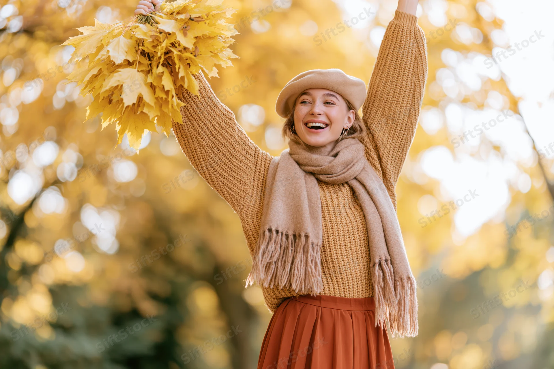 Woman laughing with arms raised holding yellow leaves in autumn park