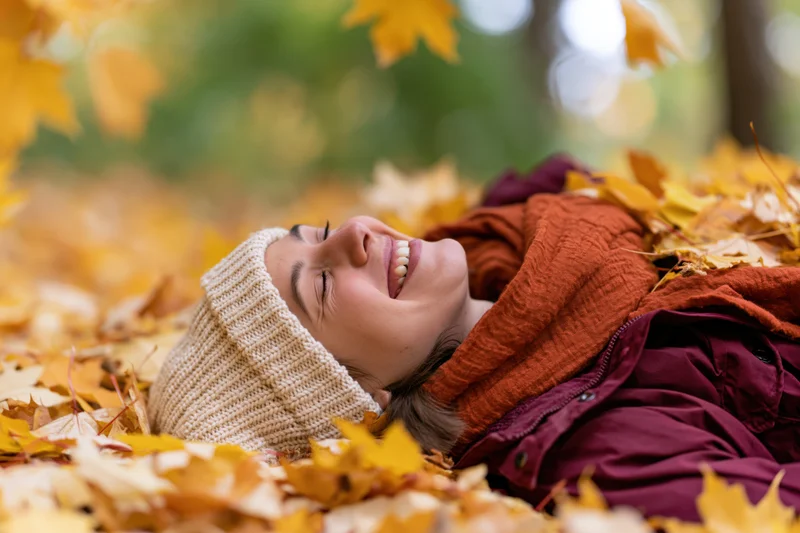 Young woman laughing while lying on her back in a pile of autumn leaves in a park