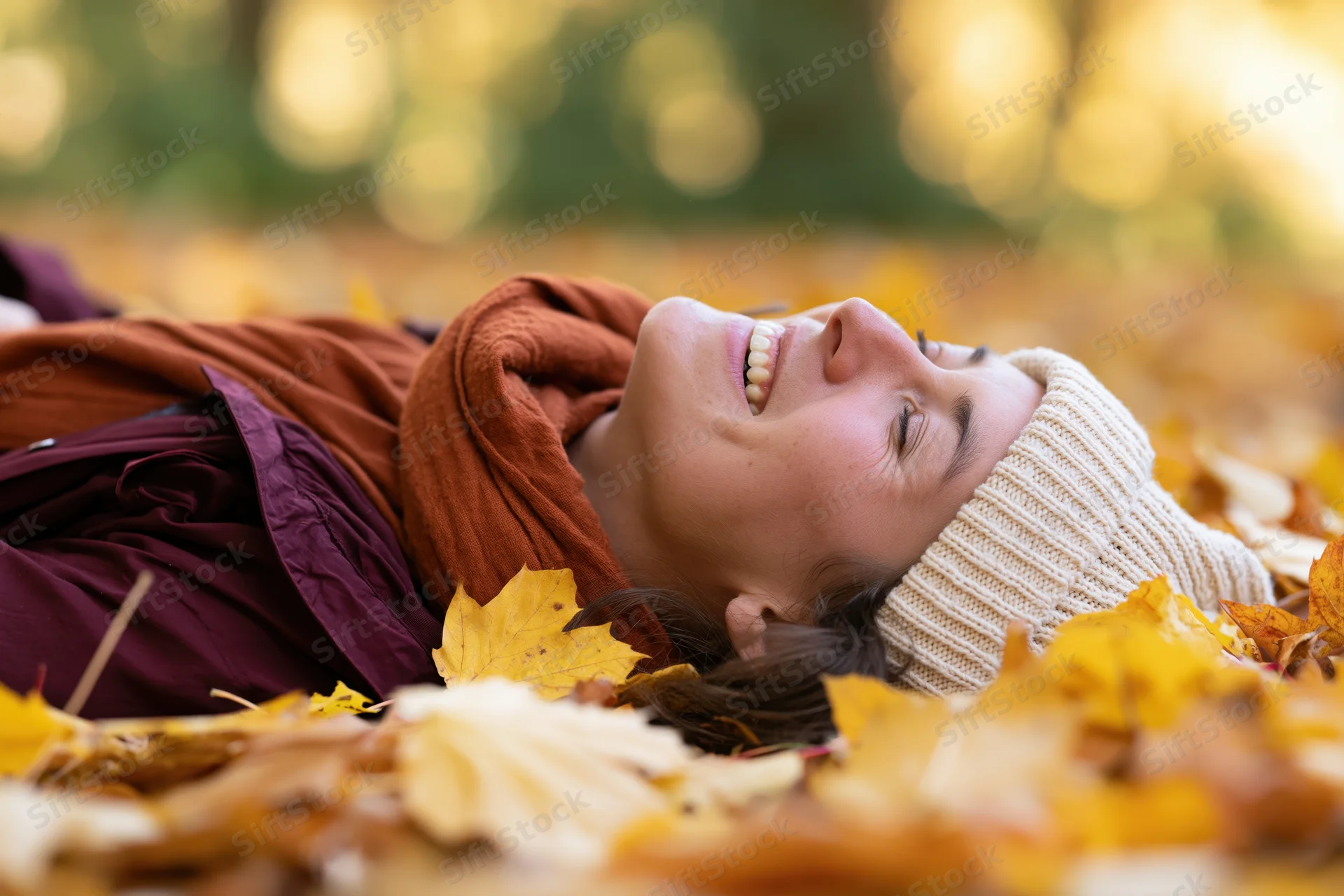 Woman lying on her back in autumn leaves laughing with eyes closed in a forest setting